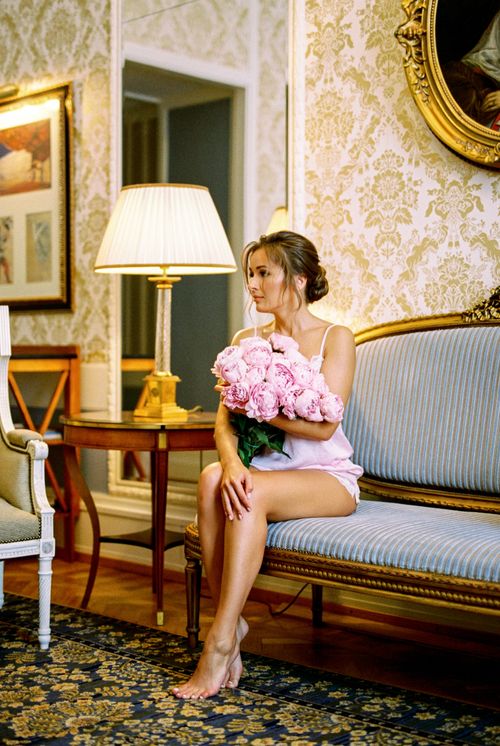 Free A woman in a vintage room holding a bouquet of pink peonies, sitting elegantly on a sofa. Stock Photo