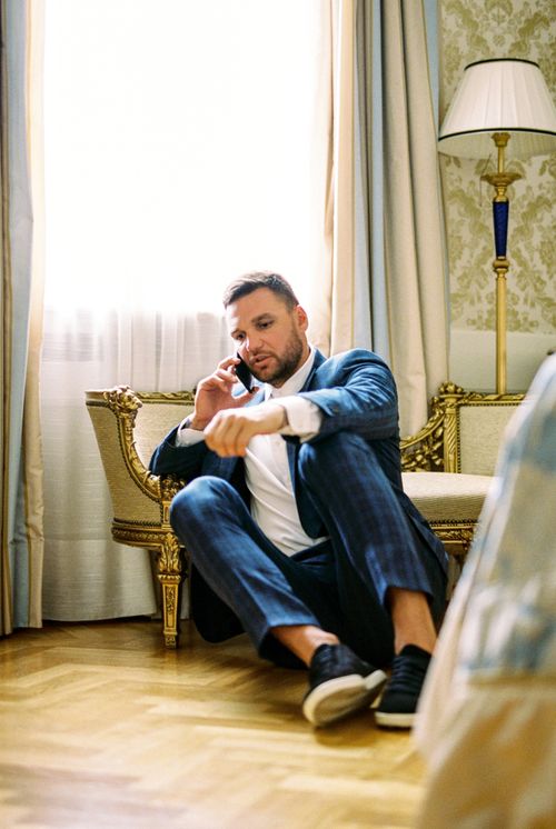 Free A man in a stylish suit sits on the floor talking on a smartphone in a luxurious room. Stock Photo