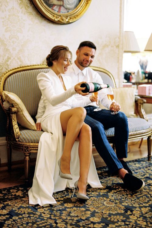 Free Newlywed couple sitting on a sofa, sharing champagne in a beautifully decorated room. Stock Photo