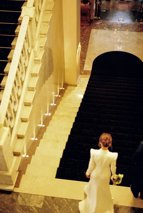 Free A bride in a white dress descends a grand staircase, highlighting elegance and wedding fashion. Stock Photo