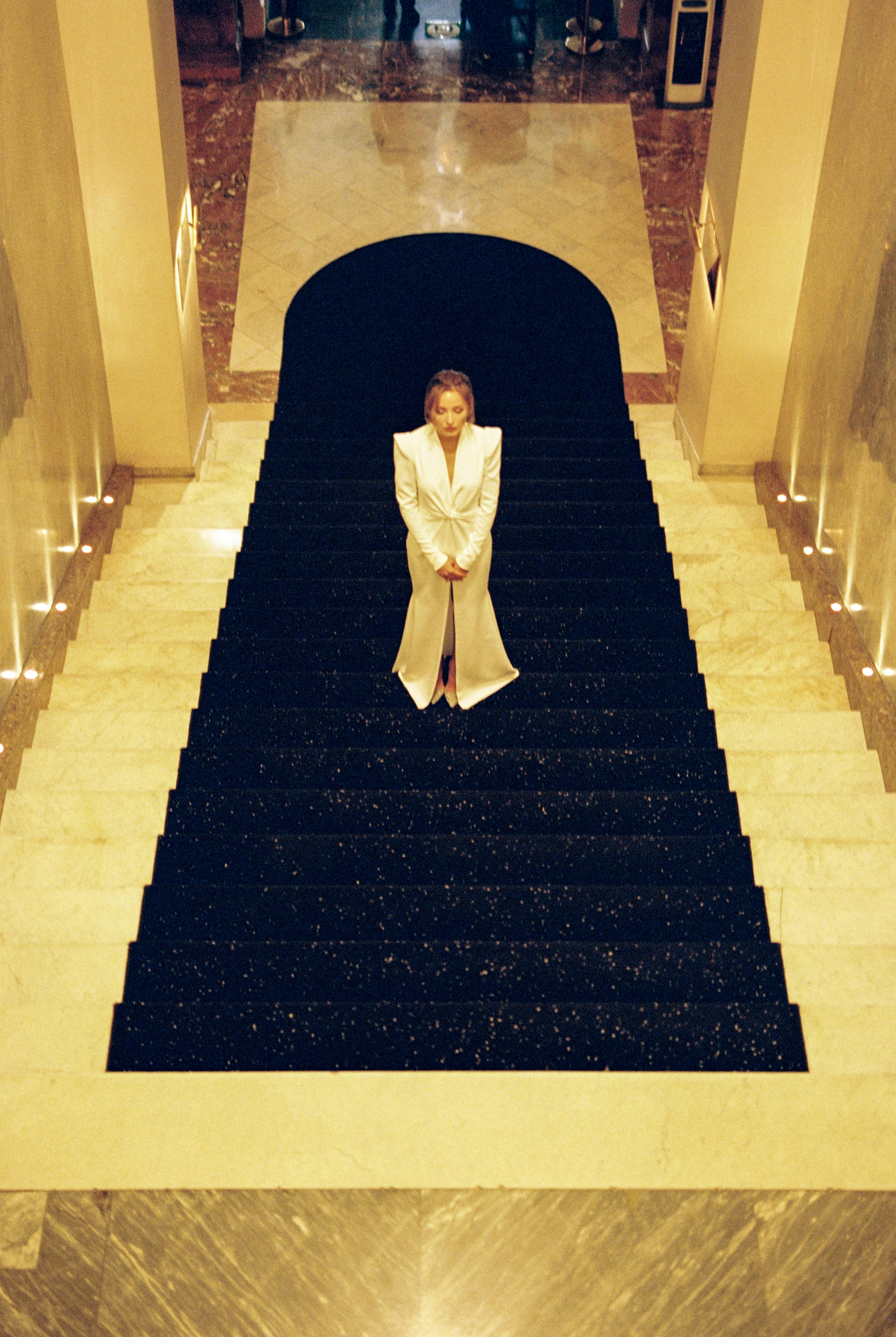 Free High-angle view of a woman in a maxi dress standing on a luxurious carpeted staircase. Stock Photo