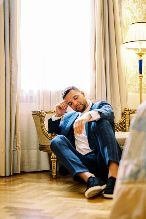 Free Man in blue suit sitting against an ornate couch, looking stressed in elegant indoor setting. Stock Photo