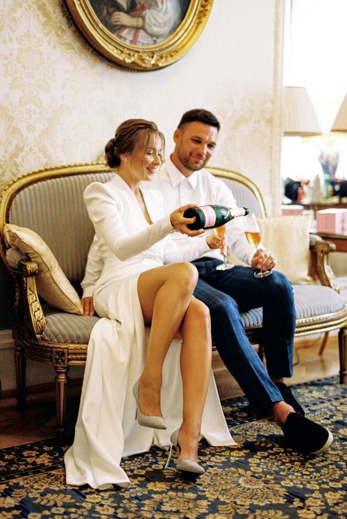 Free Bride and groom celebrate their wedding indoors with champagne, seated on a vintage sofa. Stock Photo