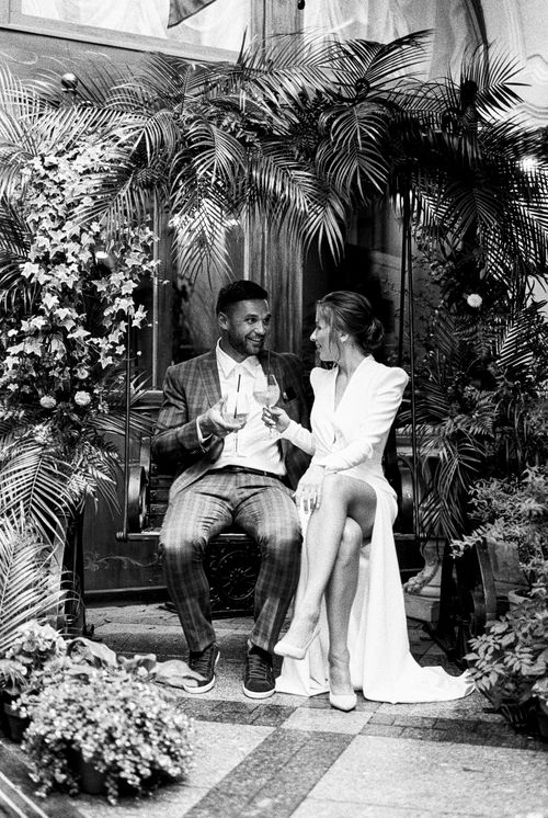 Free A stylish black and white wedding portrait of a couple sitting among lush plants, smiling and celebrating. Stock Photo