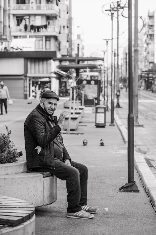Black and White Photo of Man Waiting at Bus Stop