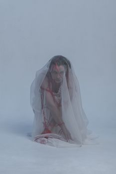 A dramatic studio photo of a woman posed with sheer fabric and red strings, evoking mystery and art.