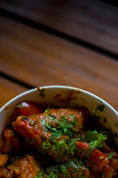 Close-up of flavorful chicken curry garnished with fresh herbs in bowl on wooden table.