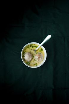 Top view of delicious creamy meatball soup in a white bowl on a dark tablecloth.