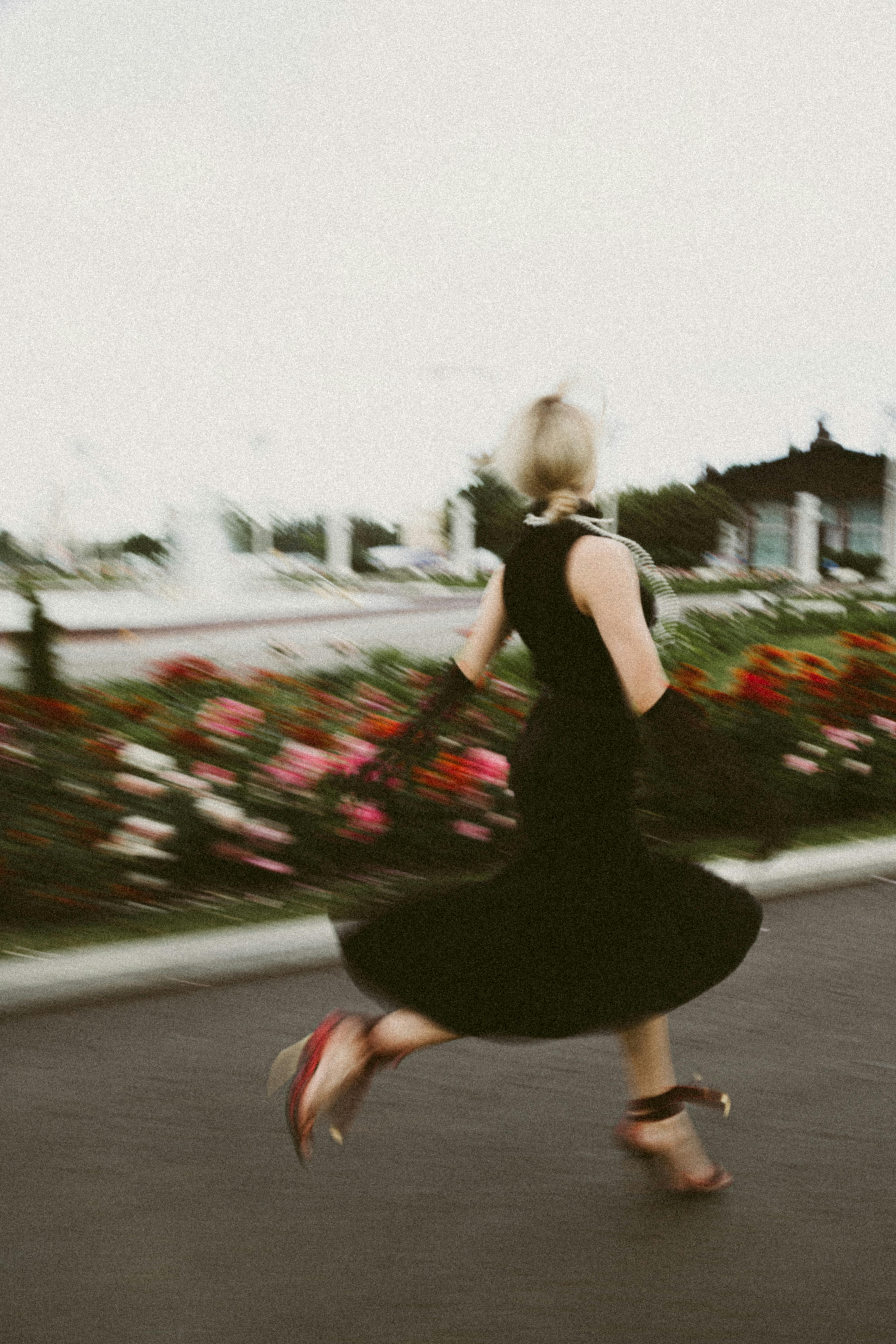 A woman in a black dress running with motion blur in a vibrant outdoor scene.