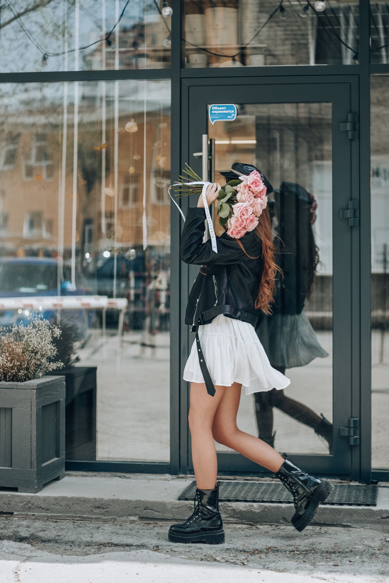 Woman in a black leather jacket, white mini skirt and platform boots holding roses