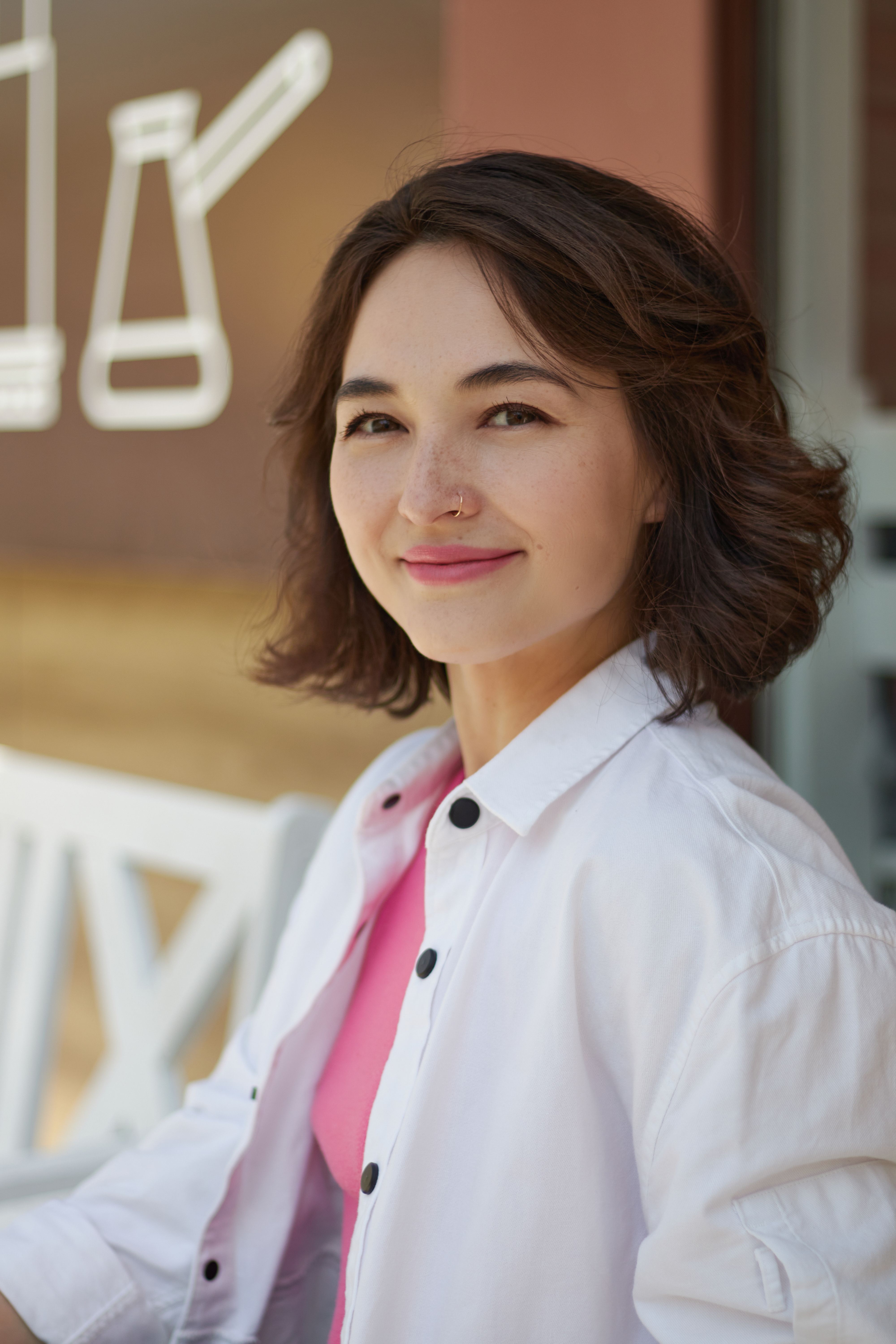 A smiling woman in casual clothing, sitting outdoors with a friendly expression.