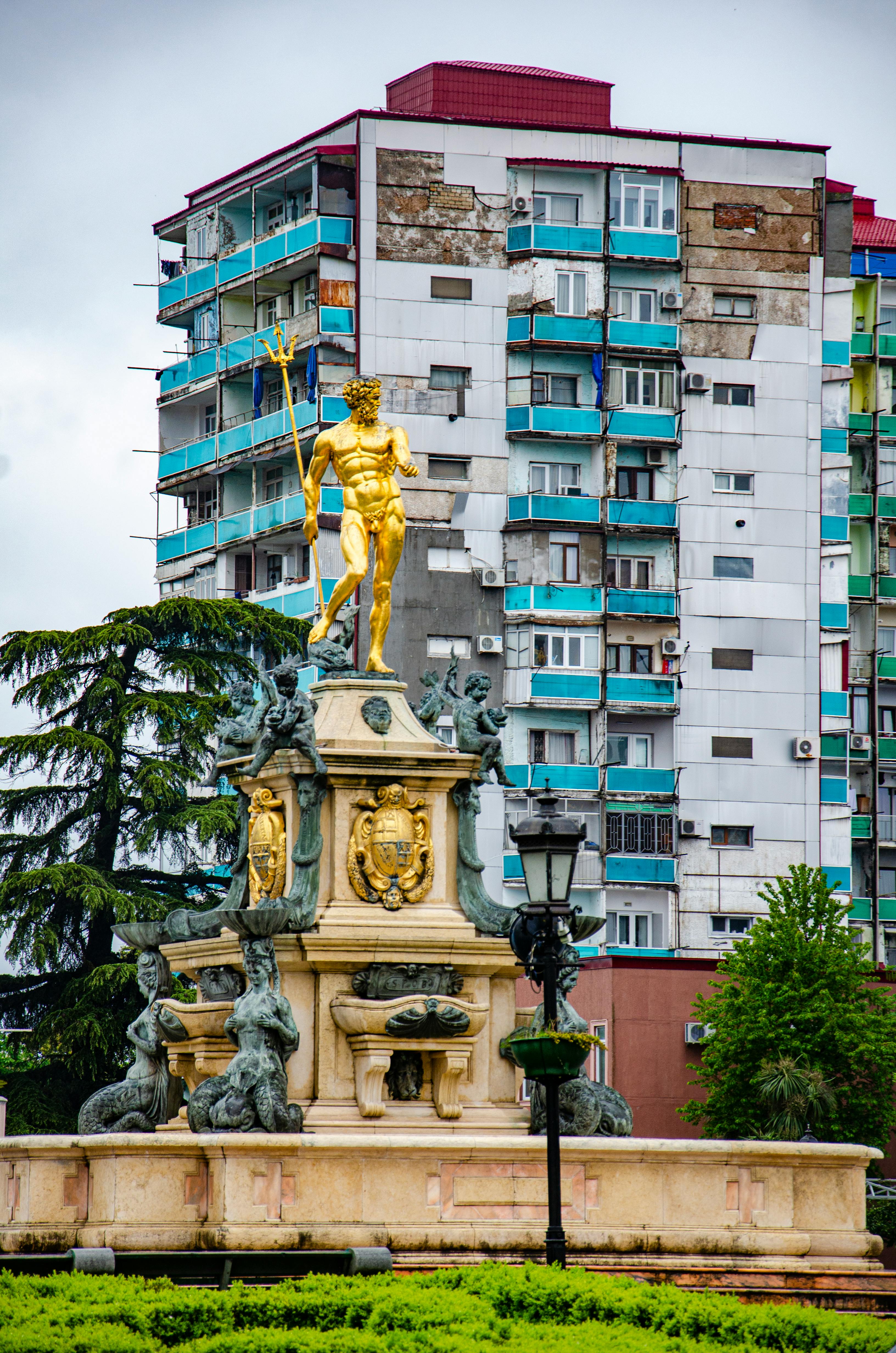 gold statue near green trees and white concrete building