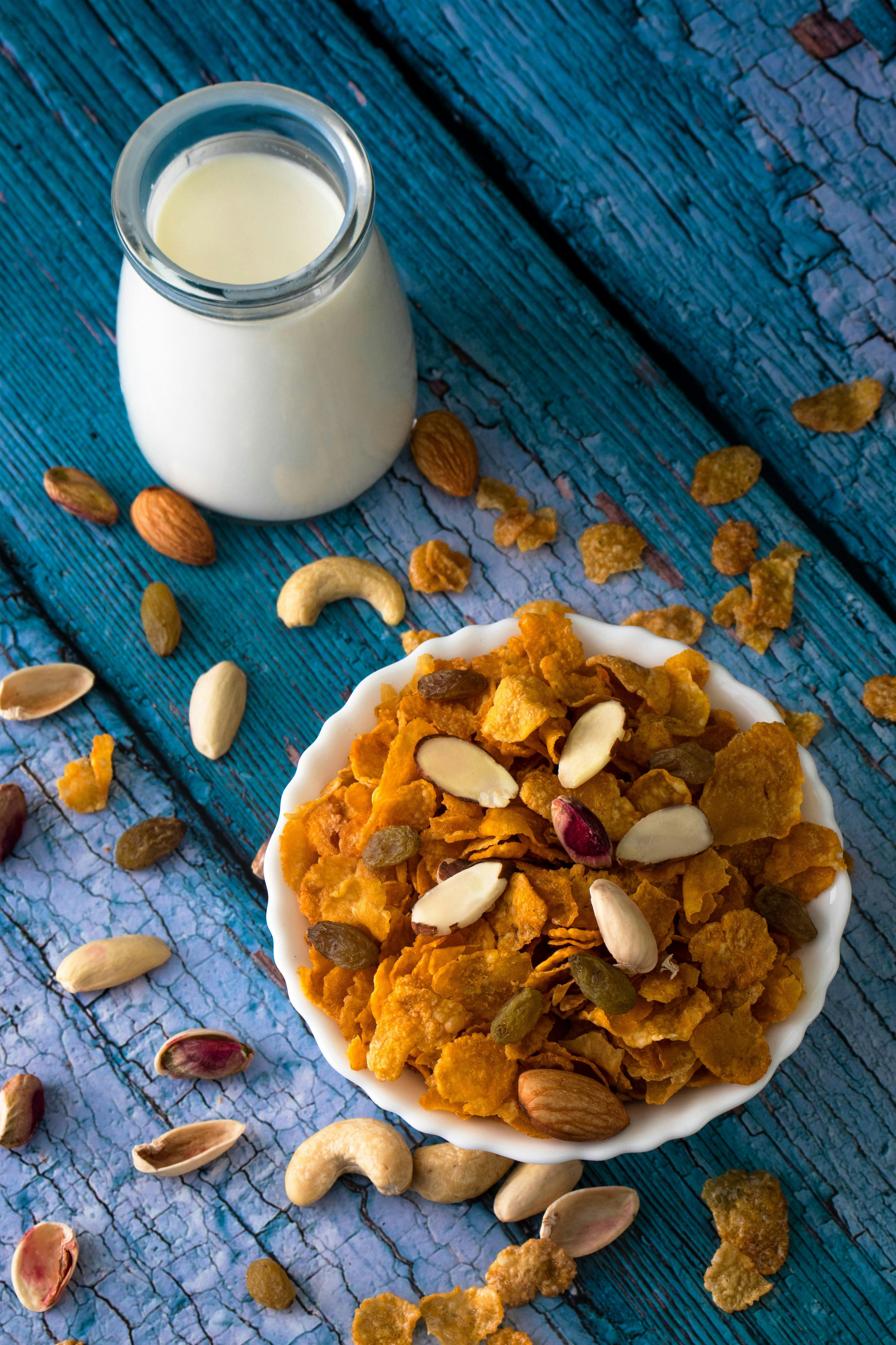 A bowl of cornflakes with almonds and milk on a rustic blue table.