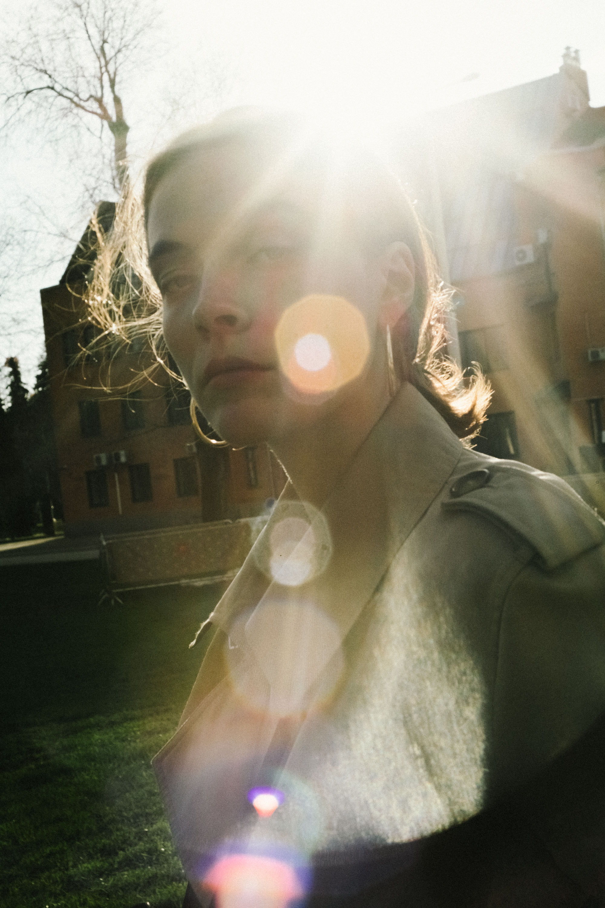 A woman stands in a sunlit courtyard with lens flare highlighting her silhouette.