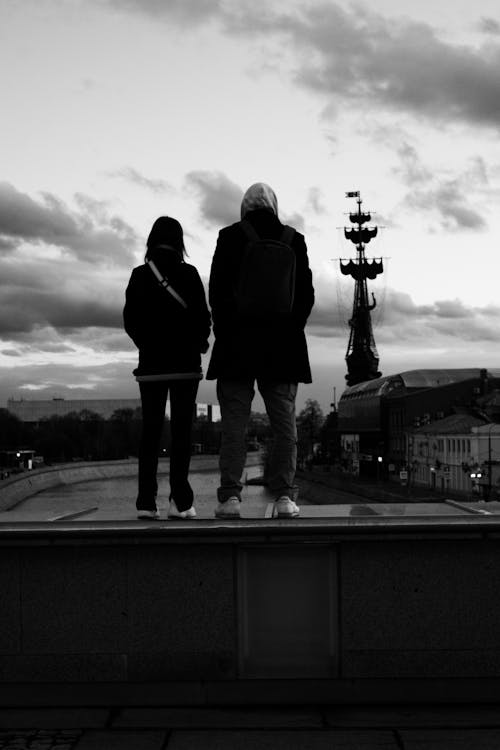 Grayscale Photo of Couple Standing on a Bridge