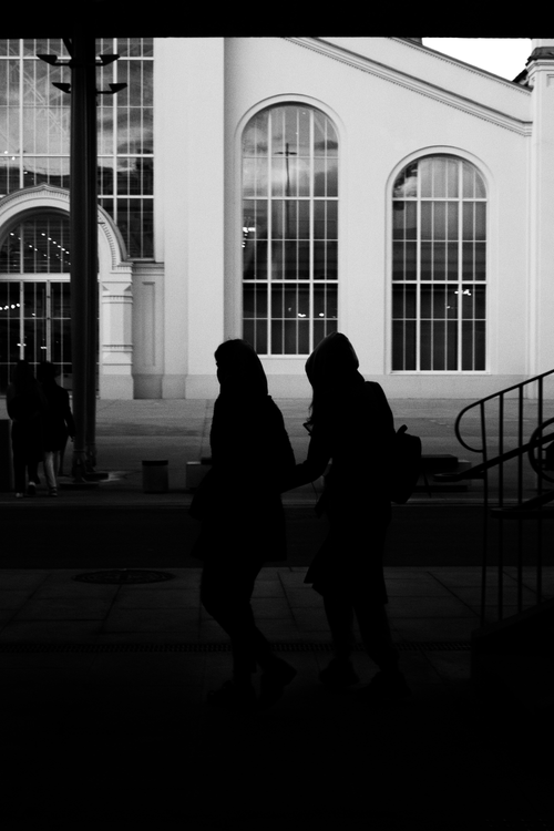 Free Silhouetted people walking near large arched windows of a modern building. Stock Photo