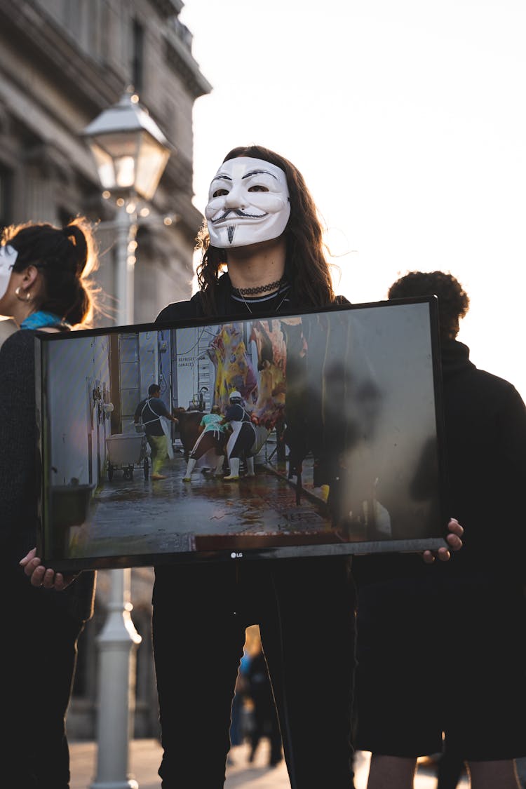 A Man In A Mask Holding A TV Set