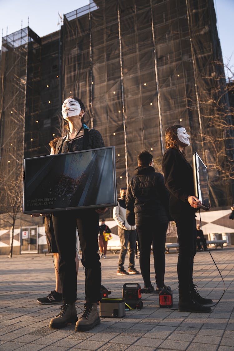 Group Of People In Protest Wearing Anonymous Masks Holding Television Sets