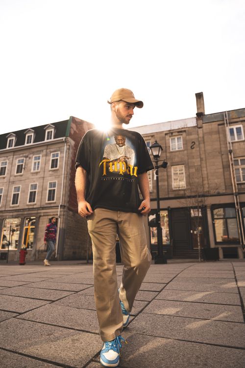 Free Stylish man wearing a graphic t-shirt and cap, illuminated by sunlight in an urban environment. Stock Photo