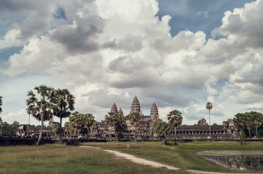 Stunning view of Angkor Wat surrounded by palm trees under a dramatic cloudy sky.