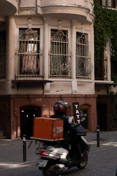 Delivery driver on a motorbike passing a historic building in Istanbul, Turkey.