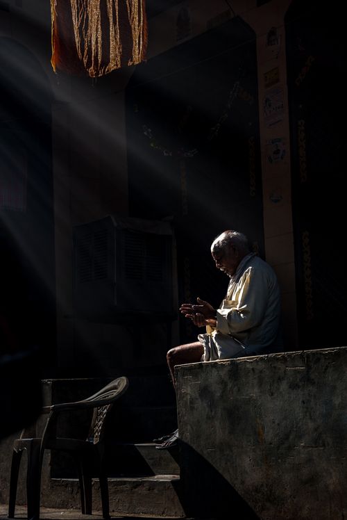 Free An elderly man sitting in deep thought as sunlight beams down on him in a traditional Delhi setting. Stock Photo