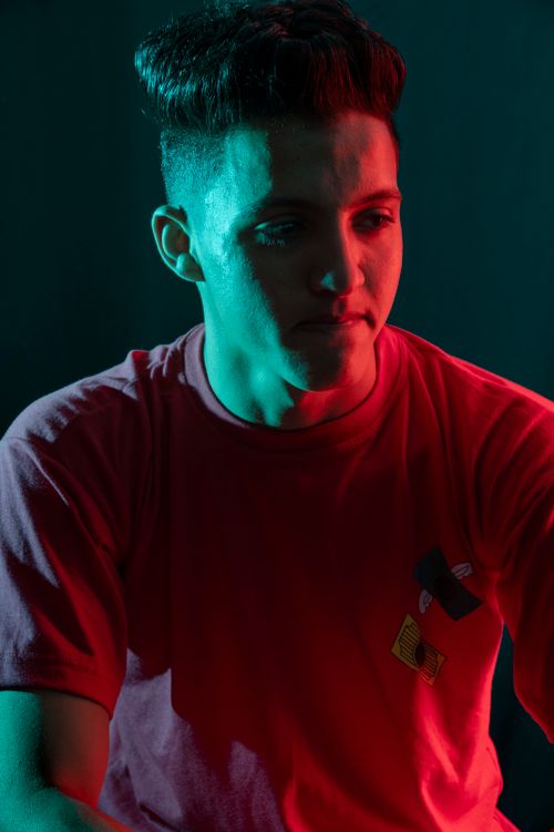Free Portrait of a young man in a red t-shirt, illuminated by dramatic colored lighting against a dark background. Stock Photo