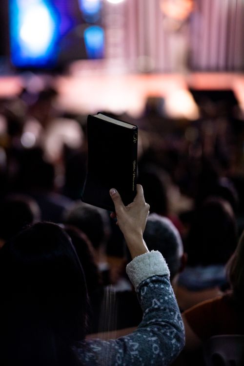 Free A person holds up a Bible during an indoor religious gathering, highlighting faith. Stock Photo