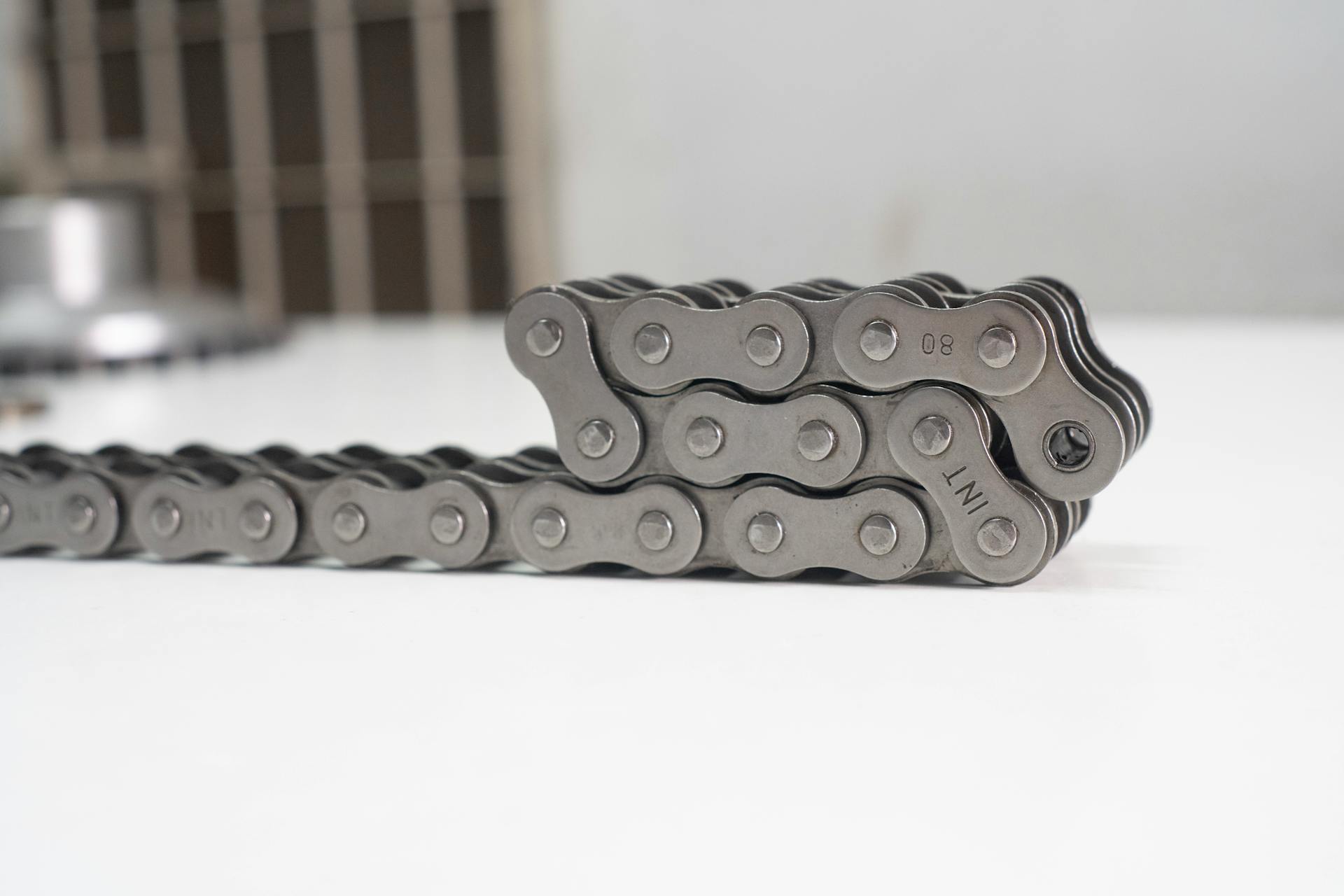 Detailed close-up of a motorcycle chain with metal links on a white surface, perfect for mechanical themes.