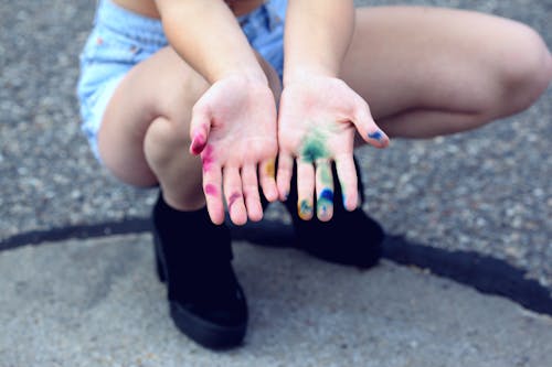 бесплатная Женщина сидит на корточках, протягивая руки с разными красками Стоковое фото