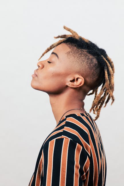 Side profile portrait of a young non-binary individual with dreadlocks against a neutral studio background.
