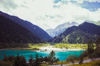 在多云的天空下，绿松石山湖被郁郁葱葱的森林和雄伟的山峰环绕，景色壮丽