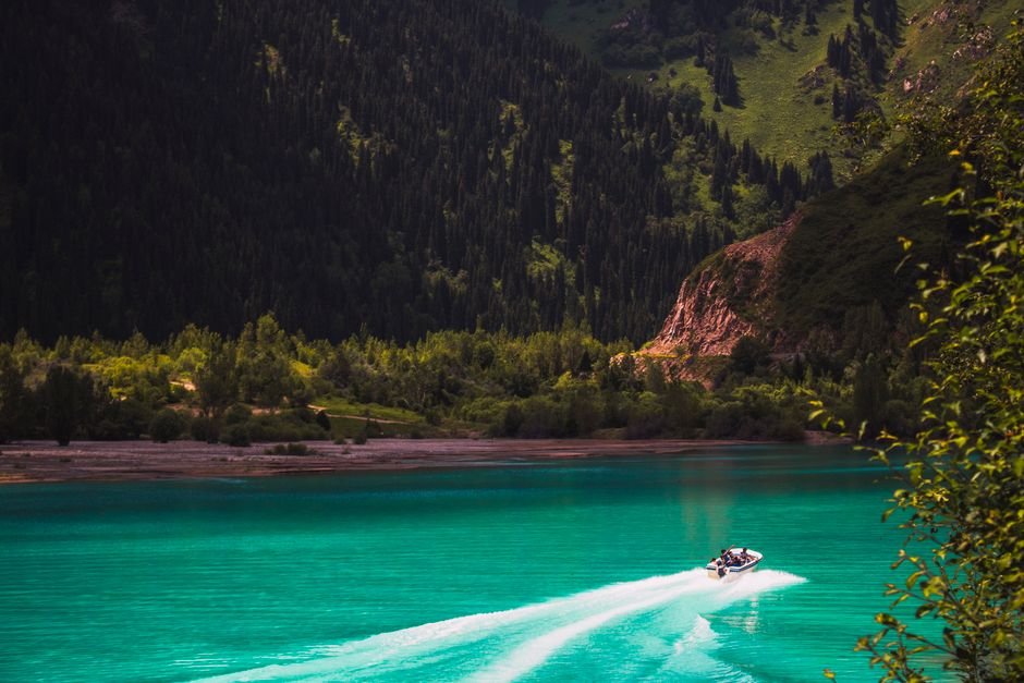 A speedboat cruises on a turquoise lake surrounded by lush forested hills. Perfect for travel lovers.