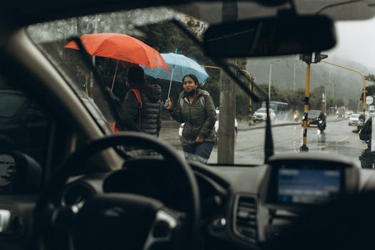 View through car windshield of people with umbrellas on a rainy street.