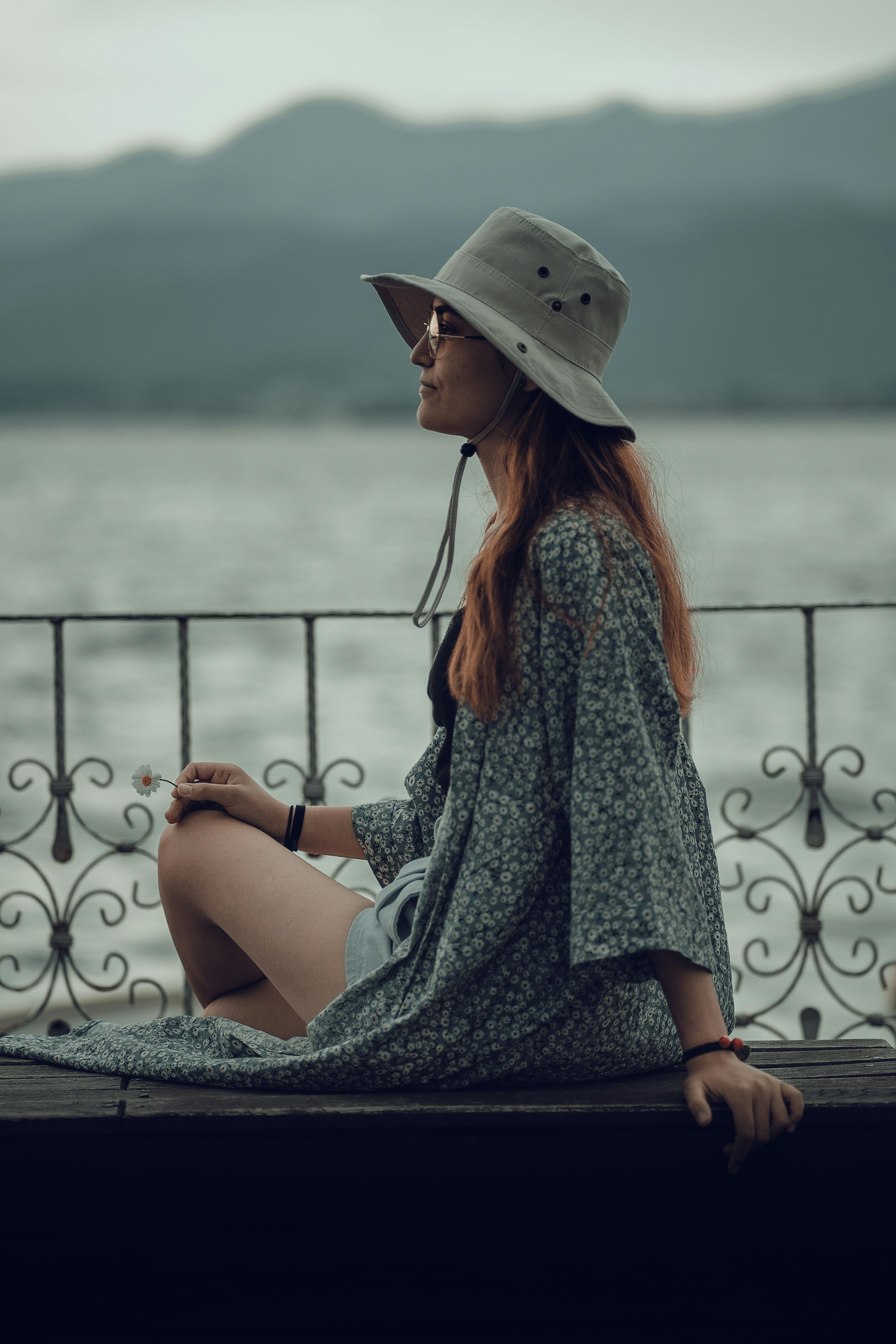 Free A woman in a sun hat sits by a lake, embracing a peaceful summer day. Stock Photo