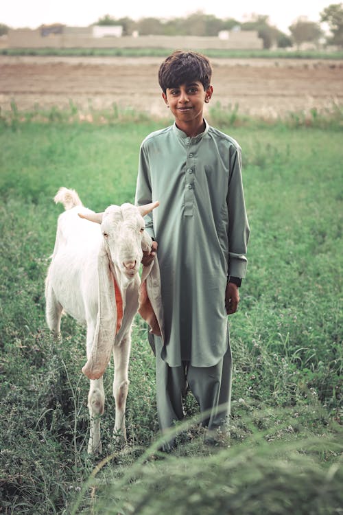 A Boy Standing Beside the White Goat