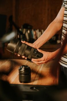Close-up of hands holding camera lens on wooden table indoors