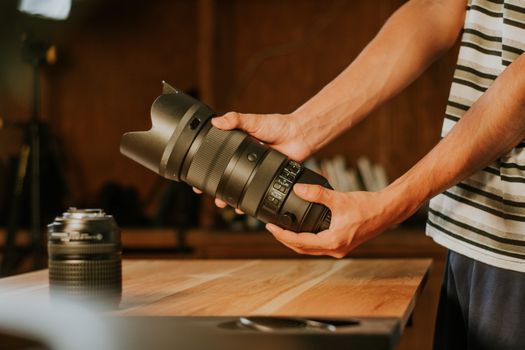 Close-up of a man holding a large camera lens in a warmly lit indoor setting.