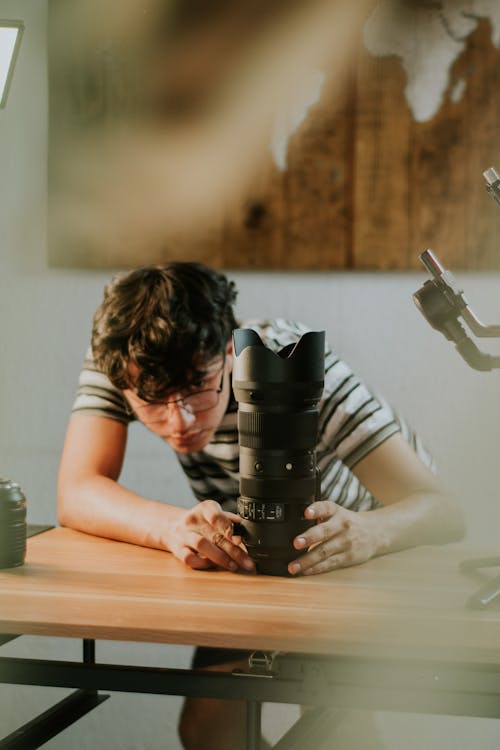 Man Wearing Eyeglasses Holding the Camera Lens on Table 