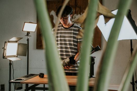 Photographer setting up lights in studio with equipment. Captured through foliage.