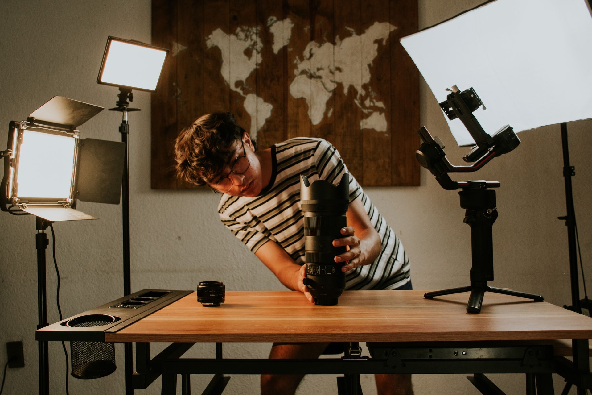 A photographer preparing camera gear in a studio with professional lighting setup and lens.