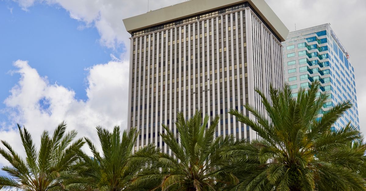 Tall skyscraper in Tampa with palm trees against a cloudy sky.