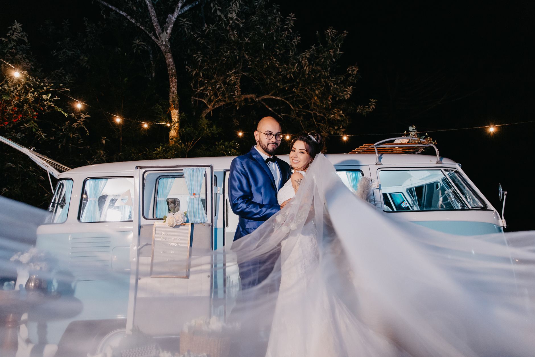 Newlywed couple posing by retro van under night lights. Perfect wedding moment capture.