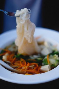 Close-up of a delicious noodle dish garnished with fresh vegetables in a white bowl.