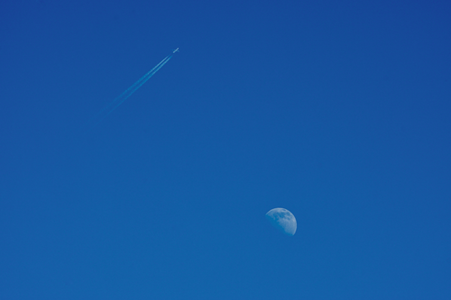 Free Airplane flying high above with the moon in a clear blue sky. Stock Photo