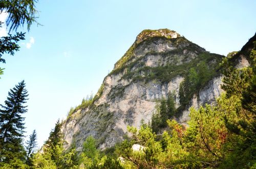 Free Stunning view of a towering mountain cliff with lush greenery under a clear blue sky. Stock Photo