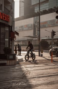 A man rides a bicycle on a bustling city street near commercial buildings and pedestrians.
