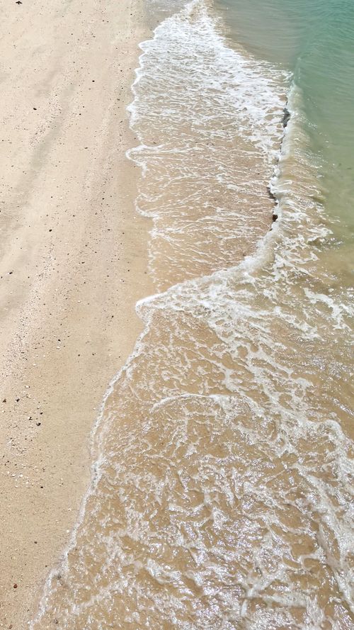 Free Aerial view of a sandy beach with gentle waves lapping the shore on a sunny day. Stock Photo