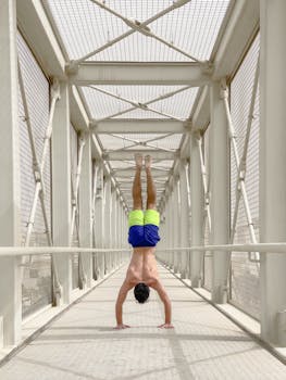Athletic man performs a handstand in a symmetrical bridge structure.