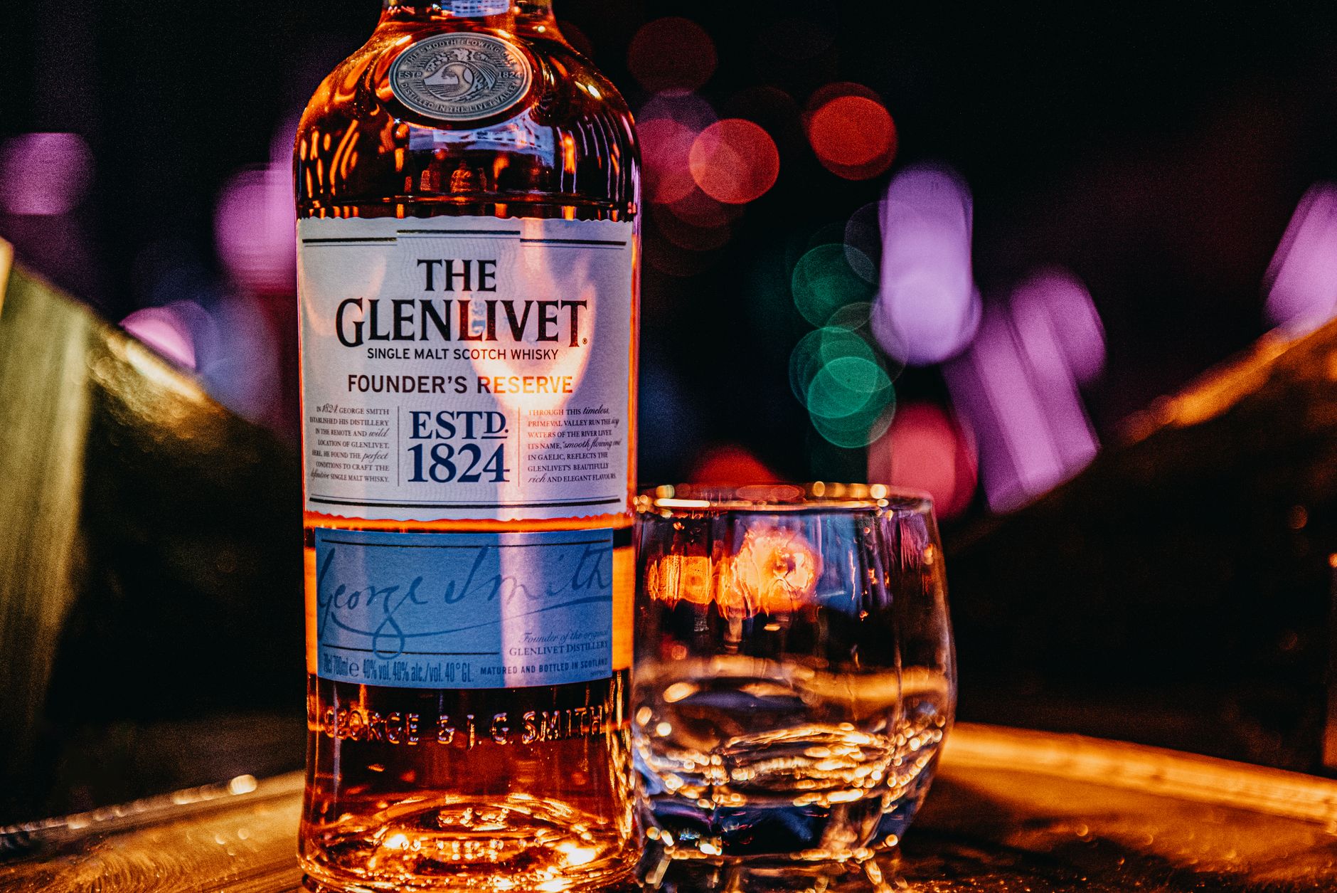 A crystal tumbler of amber Scotch whisky held against warm golden light, showcasing the spirit's rich color and clarity.